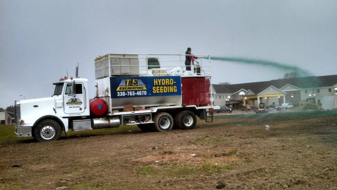 T&E hydroseeding truck spraying a commercial lot at dusk